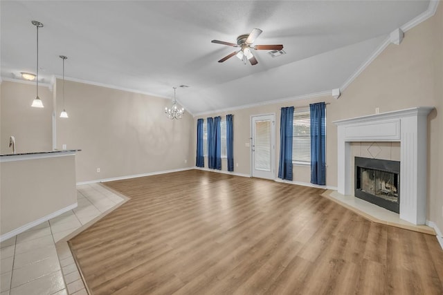 unfurnished living room featuring visible vents, vaulted ceiling, a tiled fireplace, crown molding, and ceiling fan with notable chandelier