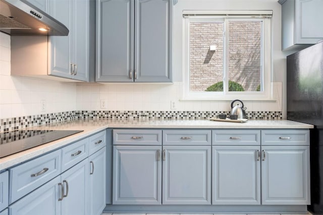 kitchen with under cabinet range hood, black appliances, light countertops, and tasteful backsplash