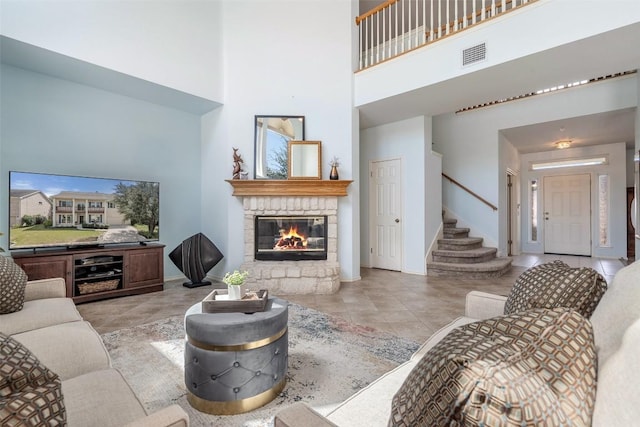 tiled living area with visible vents, baseboards, stairway, a high ceiling, and a glass covered fireplace