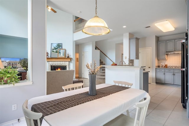 dining space with stairway, light tile patterned floors, visible vents, ceiling fan, and a stone fireplace