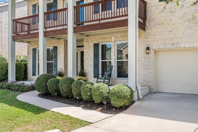 doorway to property with stone siding, an attached garage, and concrete driveway