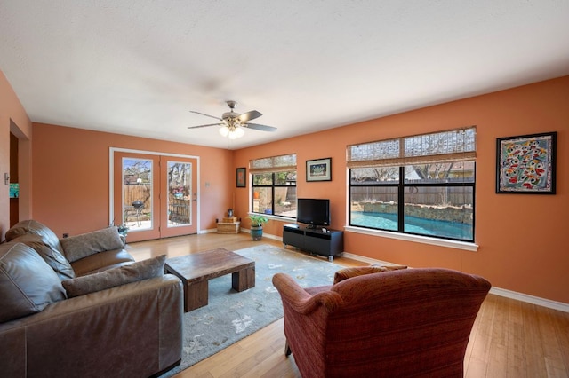 living area with hardwood / wood-style floors, a ceiling fan, and baseboards