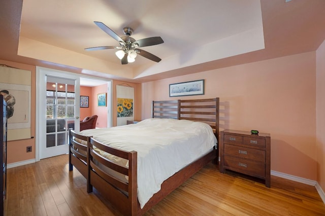 bedroom featuring baseboards, a raised ceiling, a ceiling fan, and light wood finished floors