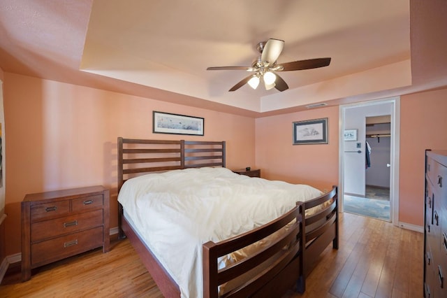 bedroom with visible vents, a walk in closet, baseboards, light wood-type flooring, and a raised ceiling