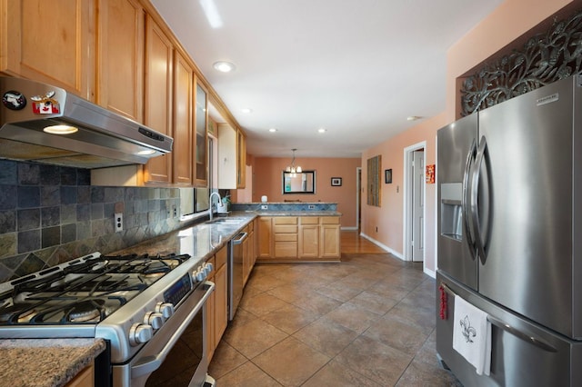 kitchen with under cabinet range hood, a sink, backsplash, appliances with stainless steel finishes, and a peninsula