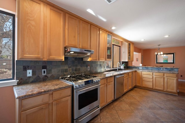 kitchen featuring backsplash, under cabinet range hood, a peninsula, stainless steel appliances, and a sink