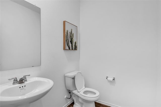 half bathroom featuring wood finished floors, toilet, baseboards, and a sink