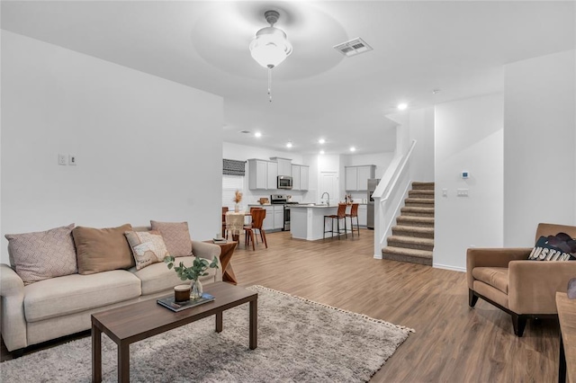 living room featuring visible vents, stairway, light wood finished floors, baseboards, and ceiling fan