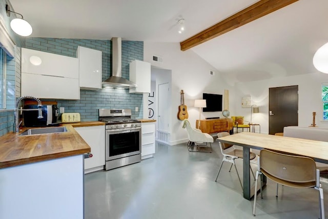 kitchen with wall chimney range hood, butcher block counters, stainless steel gas stove, white cabinetry, and a sink