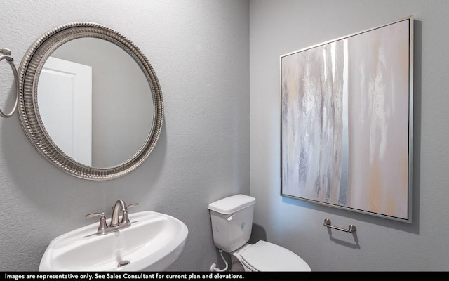 bathroom with toilet, a textured wall, and a sink