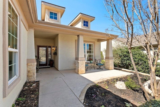 view of exterior entry with stucco siding and a porch