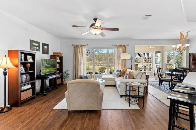 living area with wood finished floors, crown molding, ceiling fan with notable chandelier, and visible vents