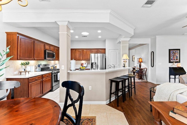 kitchen featuring a breakfast bar, decorative columns, visible vents, and appliances with stainless steel finishes