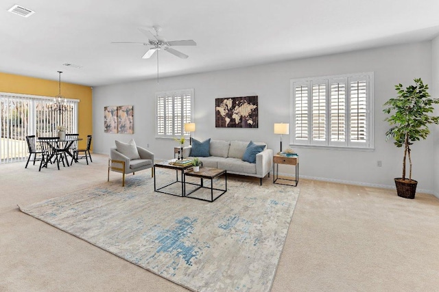 carpeted living room featuring ceiling fan with notable chandelier, visible vents, and baseboards