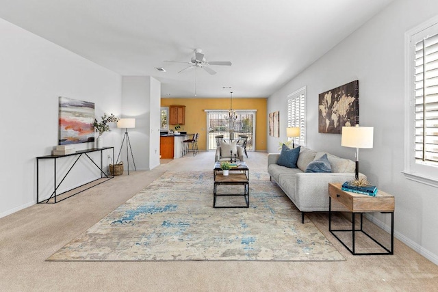 living room with baseboards, light colored carpet, and ceiling fan with notable chandelier