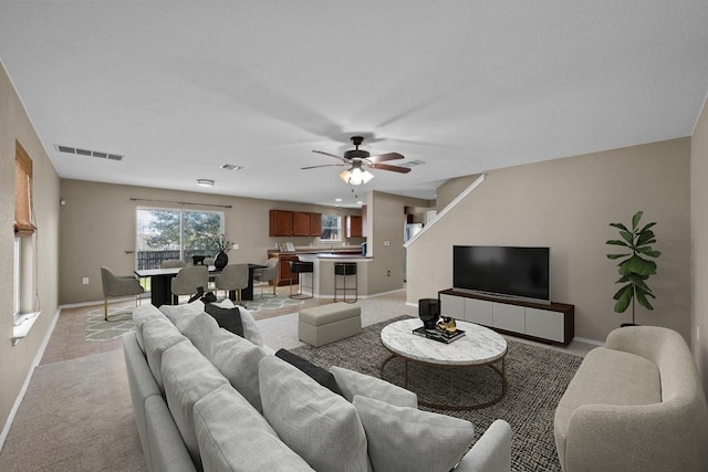 living room featuring visible vents, light carpet, baseboards, and a ceiling fan