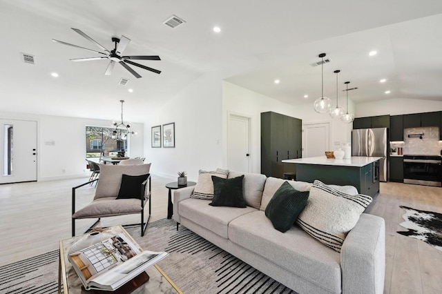 living area featuring ceiling fan with notable chandelier, lofted ceiling, light wood-style floors, and visible vents