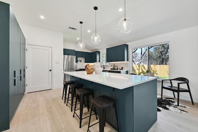 kitchen with light countertops, lofted ceiling, a kitchen breakfast bar, freestanding refrigerator, and light wood-style floors