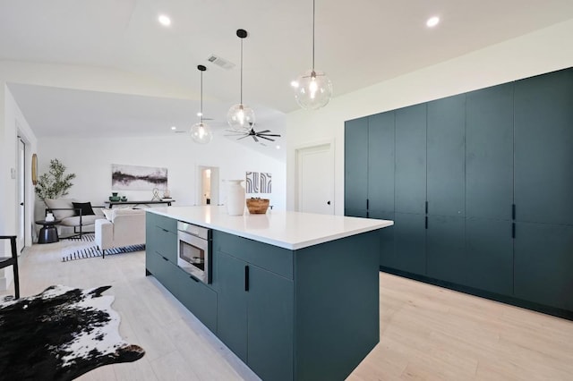 kitchen featuring visible vents, stainless steel microwave, a center island, light wood-style floors, and lofted ceiling