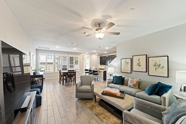 living room with visible vents, baseboards, ceiling fan, light wood-style floors, and a textured ceiling