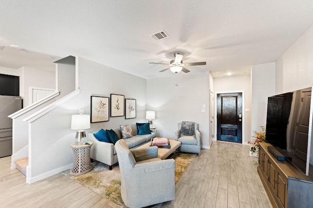 living area with visible vents, a ceiling fan, light wood finished floors, baseboards, and stairs