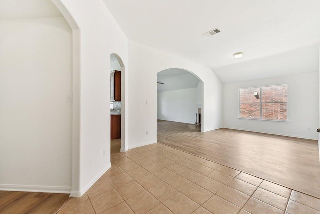 spare room with visible vents, arched walkways, light wood finished floors, baseboards, and vaulted ceiling