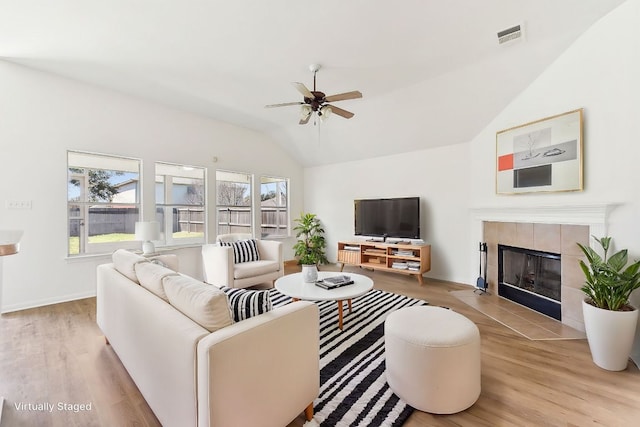 living room with visible vents, a tiled fireplace, a ceiling fan, wood finished floors, and vaulted ceiling