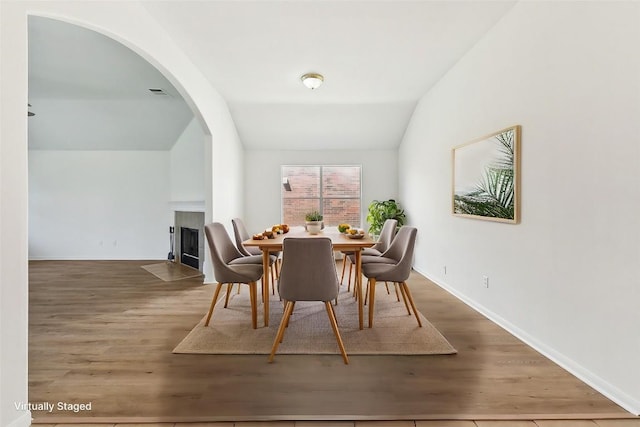 dining room featuring arched walkways, visible vents, lofted ceiling, and wood finished floors