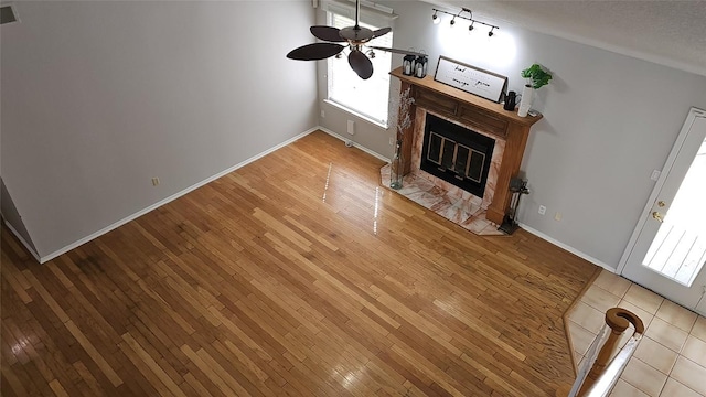 unfurnished living room featuring a ceiling fan, a textured ceiling, wood-type flooring, a fireplace, and baseboards