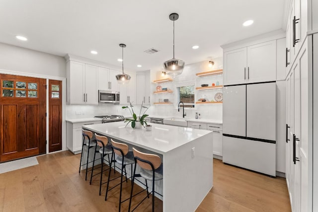 kitchen with a breakfast bar area, visible vents, open shelves, freestanding refrigerator, and stainless steel microwave