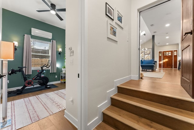 stairs with baseboards, an AC wall unit, a ceiling fan, and wood finished floors