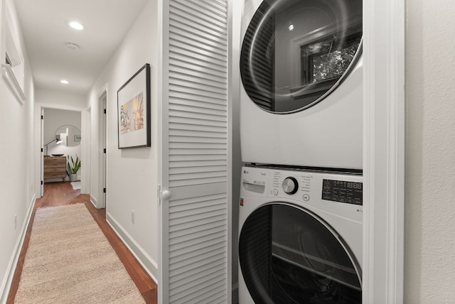 clothes washing area with stacked washer and clothes dryer, wood finished floors, recessed lighting, baseboards, and laundry area