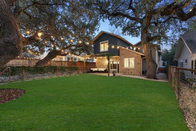 back of house featuring a yard, stone siding, and a fenced backyard