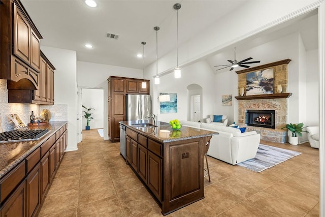 kitchen featuring visible vents, appliances with stainless steel finishes, a fireplace, arched walkways, and a ceiling fan