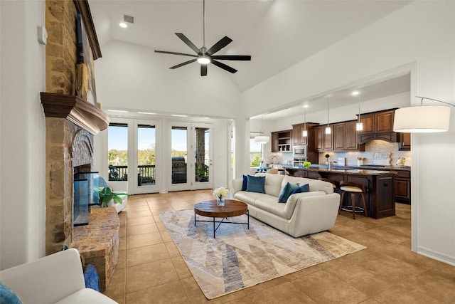 living room with visible vents, light tile patterned floors, a stone fireplace, high vaulted ceiling, and a ceiling fan