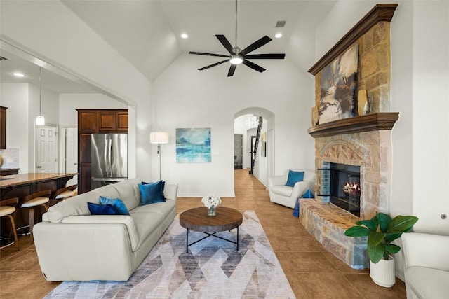 living room with high vaulted ceiling, a ceiling fan, arched walkways, a fireplace, and light tile patterned floors