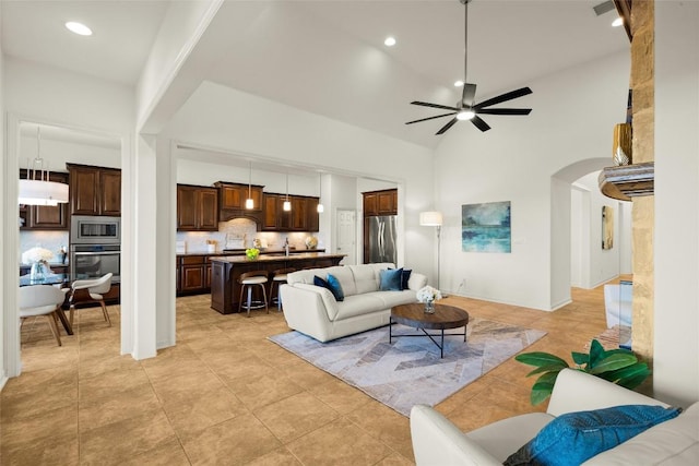 living room featuring light tile patterned flooring, recessed lighting, arched walkways, ceiling fan, and a towering ceiling