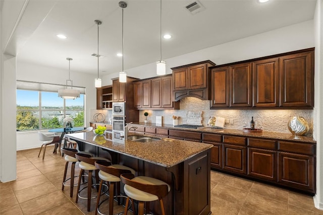 kitchen featuring visible vents, decorative backsplash, dark stone countertops, stainless steel appliances, and a sink