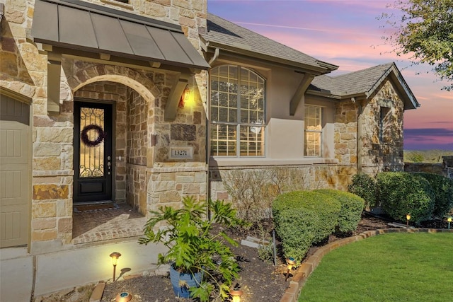 exterior entry at dusk with stone siding and a shingled roof