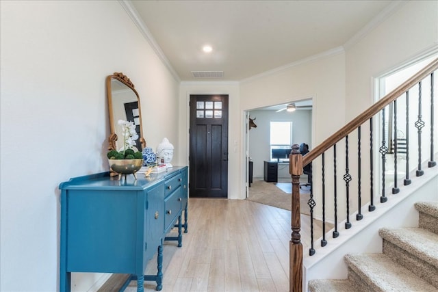 foyer featuring visible vents, light wood-style flooring, crown molding, and stairway