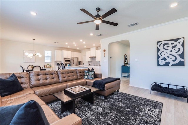 living area featuring light wood finished floors, visible vents, ceiling fan with notable chandelier, and crown molding