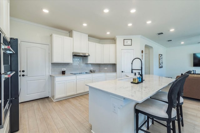 kitchen featuring visible vents, under cabinet range hood, arched walkways, light wood finished floors, and black electric cooktop