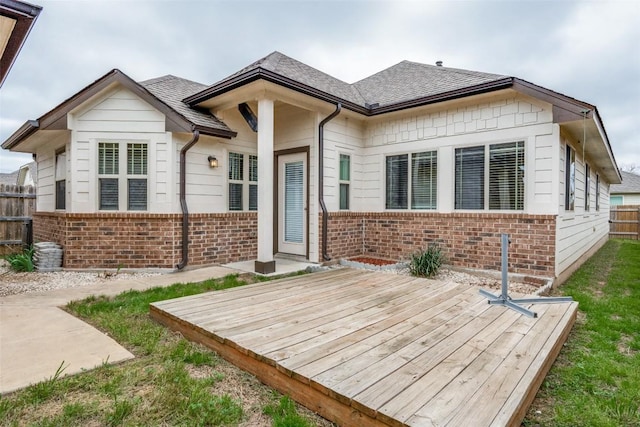 view of front of home featuring a wooden deck, fence, brick siding, and a shingled roof