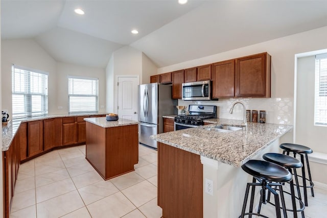 kitchen featuring brown cabinets, a sink, light stone counters, appliances with stainless steel finishes, and a peninsula