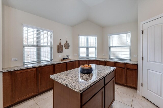 108 Trailstone Dr, Bastrop, TX 78602 - kitchen featuring light tile patterned floors, light stone countertops, lofted ceiling, brown cabinets, and a center island