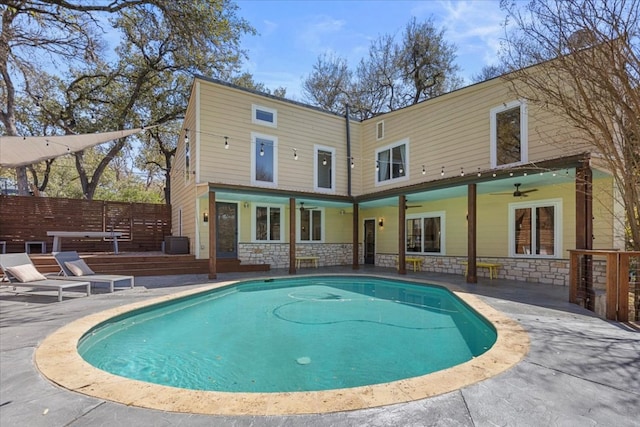 rear view of property featuring a fenced in pool, stone siding, ceiling fan, and a patio area