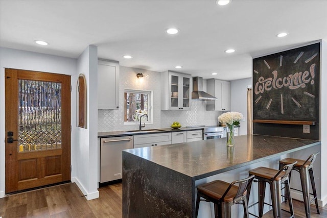 kitchen featuring dark wood-style floors, a sink, appliances with stainless steel finishes, dark countertops, and wall chimney exhaust hood