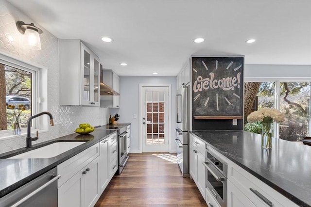 kitchen featuring a sink, backsplash, glass insert cabinets, appliances with stainless steel finishes, and dark wood-style flooring