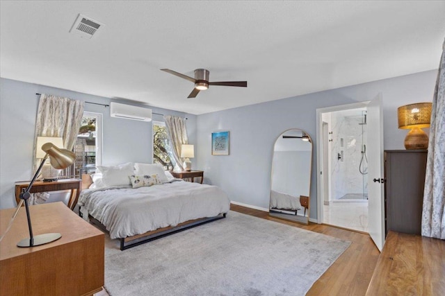 bedroom featuring visible vents, ceiling fan, a wall unit AC, ensuite bathroom, and wood finished floors