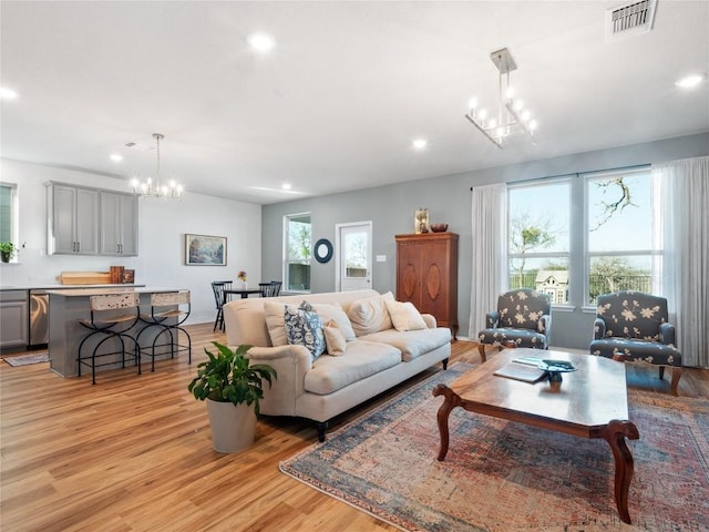 living room with a wealth of natural light, a notable chandelier, light wood-style flooring, and visible vents